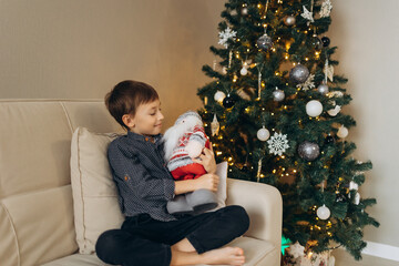 boy sitting with a toy in his hands against the background of a Christmas tree