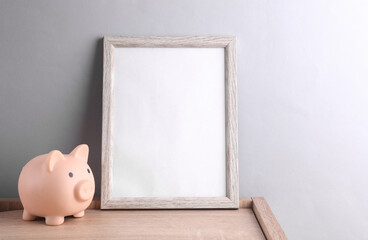 White empty photo frame with piggy bank on gray background