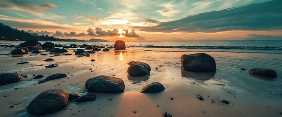 calm sea with rocks on sandy beach during sunset.