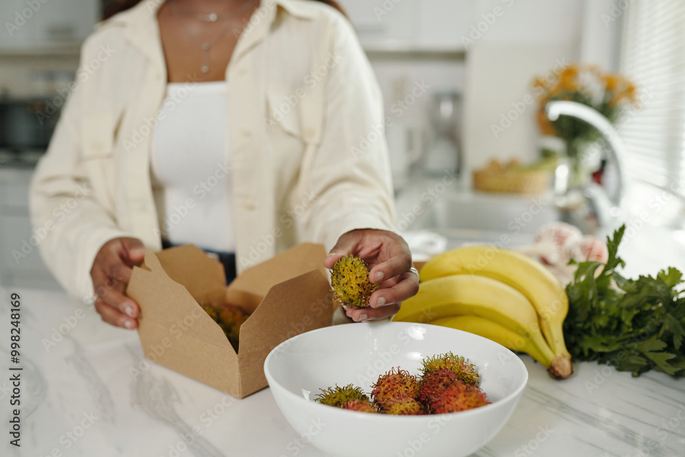 Person holding open box of fresh rambutan on kitchen counter with ...