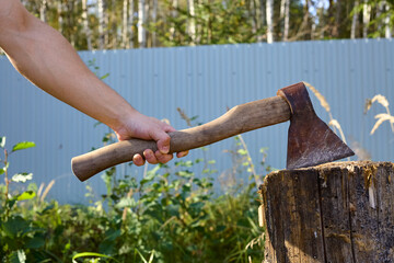 A man's hand holds an old rusty axe used for chopping firewood