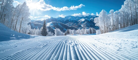 Wall Mural - Snow covered mountains with a groomed ski slope in the foreground, bright blue sky with white clouds.