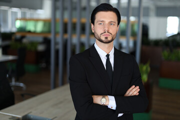 Wall Mural - A man in a suit and tie stands in front of a desk, looking confident and professional. He is wearing a watch on his wrist, which adds to his polished appearance