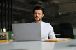 © Andrii Zastrozhnov - A man is sitting at a desk with a laptop open in front of him. He is wearing a white shirt and he is focused on his work. Concept of productivity and concentration