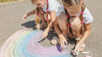 Girls drawing rainbow on sidewalk with chalk