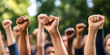 © Lila Patel - The Unyielding Strength of Resilience: A group of people standing together, their fists raised in defiance.