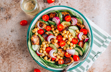 A fresh salad in a bowl featuring red onion, chickpeas, cucumber, tomatoes, grilled chicken, and baby spinach. A nutritious, vibrant dish ideal for healthy meals and quick lunches. Top view