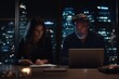 © Milos - A man and woman collaborate on a laptop in an office, with a city skyline visible outside the window, conveying dedication and teamwork in a professional setting.