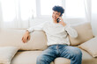 © SHOTPRIME STUDIO - smiling young man talking on smartphone, casual atmosphere, sitting on a light couch, indoor setting, natural light, comfortable and relaxed ambiance