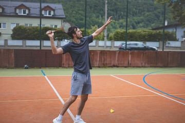 Badminton player focuses on the shuttlecock mid-air during a match on an outdoor court. With his racket raised, he prepares for the next shot, surrounded by an urban and scenic background