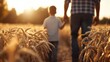 ©  Jovaduplex - The image captures a father and son holding hands and walking through a golden wheat field at sunset, symbolizing family bonding, warmth, and togetherness in nature.