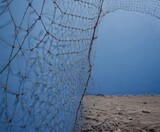 A close-up view fishing net with a sandy beach and a clear blue sky in the background