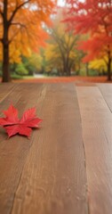 Poster - A vibrant red maple leaf rests on a wooden surface, with a blurred autumn landscape of orange, yellow, and green trees in the background