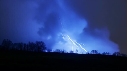 Wall Mural - Dramatic bolt of lightning lights up the dark sky, casting a glow over the countryside. Nature's power on full display, creating an ominous scene