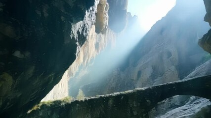 Poster - Sunlight shines through a cave, illuminating a stone bridge over glistening water, creating a captivating contrast of light and shadow in this mysterious underground landscape
