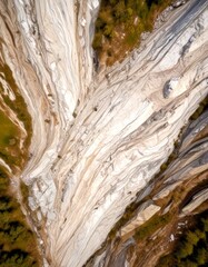 Poster - Aerial view rocky cliff face with a mix of white, gray, and brown hues, surrounded by greenery