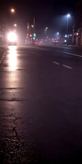 Aufkleber - A dimly lit city street at night, with a wet road reflecting the street lights and a car's headlights visible in the distance