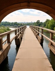 Poster - A wooden bridge with railings spans a river, framed by a wooden archway and overlooking a cityscape with trees and buildings