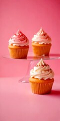 Poster - Three cupcakes with pink frosting and sprinkles are arranged on a clear glass cake stand against a pink background