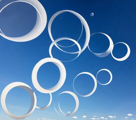 Leinwandbilder - A collection of white, circular sculptures or rings suspended against a clear blue sky, with a small moon visible in the top right corner.