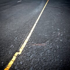 Poster - A yellow line runs diagonally across a dark asphalt road, creating a sense of depth and perspective.