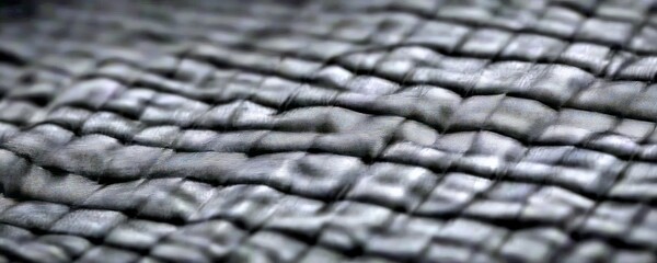 Fototapete - A close-up view textured black fabric, with a repeating pattern of small squares or rectangles that create a criss-crossing effect