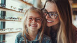© Dina Photo Stories - Happy mother and daughter trying on glasses in optic store for sight, vision or eye care at retail shop or store. Smiling young woman and girl wearing eyeglasses. Buying spectacles in optic store