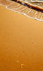 Poster - A tranquil beach scene with light brown sand, small waves, and footprints, captured from a low angle