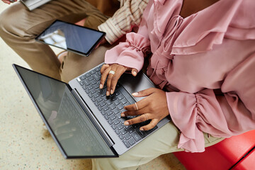 Poster - Top view of unrecognizable African American businesswoman typing on laptop keyboard sitting with male colleague on couch while working on project together