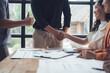 © Kritdanai - Successful Deal Closing: A handshake seals a business agreement, signifying trust and collaboration between colleagues in a modern office setting.  A thumbs-up gesture adds to the positive vibe.