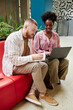 © Seventyfour - Vertical shot of smiling African American female mentor assisting male colleague in professional development, while man taking notes in notebook sitting on couch in modern office center