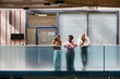 © Seventyfour - Wide angle shot of diverse group of three colleagues cheerfully chatting during break while standing on balcony in sunlight casting through glass ceiling in modern business center, copy space