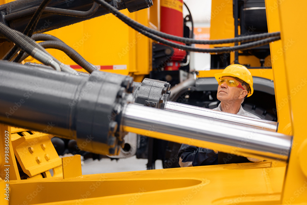 Professional mechanic checks hydraulic hose system equipment on excavator to raise bucket.