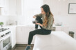© CM Photo - A woman eating a premade lunch while sitting on the counter in a bright white kitchen.