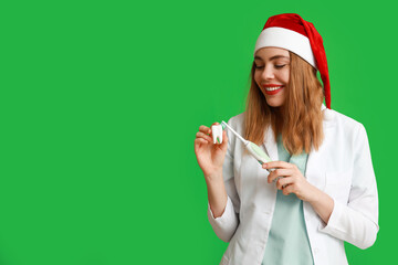 Poster - Portrait of young female dentist in Santa hat with tooth model and electric toothbrush on green background