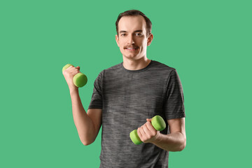 Young male fitness trainer with dumbbells on green background