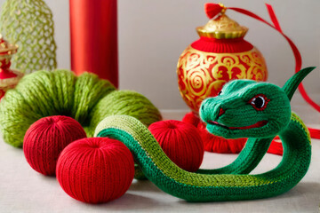 Wall Mural - Knitted green snake surrounded by red knitted balls and Chinese decorations. Symbol of New Year 2025 according to Chinese calendar handmade