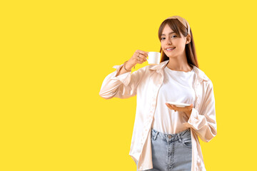 Wall Mural - Beautiful young woman with cup of coffee on yellow background