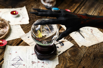 Bloody black witch hand with magic attributes and crystal ball on brown wooden background. Halloween celebration