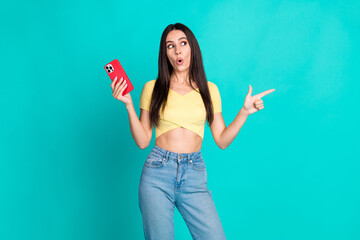 Poster - Photo of pretty young woman hold phone look direct finger empty space wear top isolated on teal color background