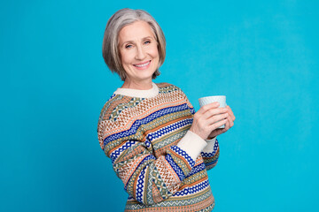 Sticker - Photo of good mood retired woman with white gray hair wear ornament sweater hold cup of cappuccino isolated on blue color background