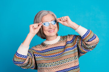 Wall Mural - Photo of cool retired woman with white gray hair wear ornament sweater fingers touching sunglass isolated on blue color background