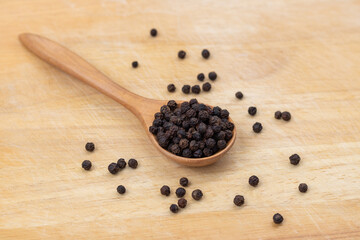 Wall Mural - Whole black pepper on a wooden spoon. Peppercorn with a wooden spoon on a wooden cutting board background. The composition is isolated from the background.