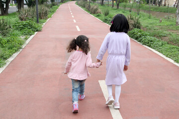 Brunette Latina 4 and 5 year old girls walk holding hands like sisters and friends spending time together outdoors