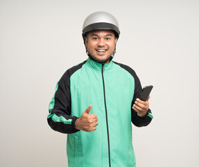 Young asian rider wearing green jacket uniform and helmet standing holding smartphone food application on isolated. Male delivery service worker. Delivery courier and shipping food service.