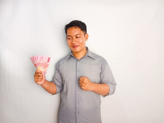 Young Asian rise up his hand while holding banknotes and shows happy expression wearing grey shirt isolated on white background