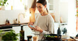 © HockleyM3/peopleimages.com - Woman, cooking and phone by stove in home for healthy salad recipe, meal prep and ingredients research. Nutrition influencer, food blogger or vegan chef with tech for social media tutorial in kitchen