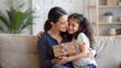 © Htet Wai Phyo - Mother's day concept. Adorable latin girl giving gift and embracing mom, mommy and daughter bonding together at home, sitting on sofa