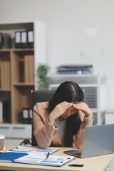 Portrait of tired young business Asian woman work with documents tax laptop computer in office. Sad, unhappy, Worried, Depression, or employee life stress concept