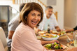 © Wavebreak Media - Smiling senior woman enjoying meal with diverse friends at dining table, sharing laughter, at home